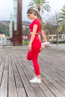 Fit woman in red outfit doing stretching in a city park, fitness and healthy active