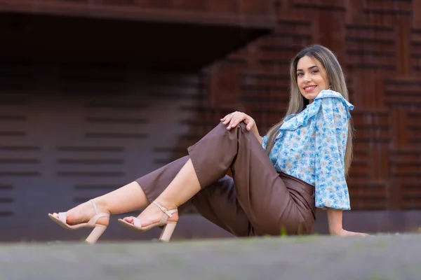 Portrait young woman sitting in the city against an iron background with brown rust, lifestyle concept, blue shirt and brown pants