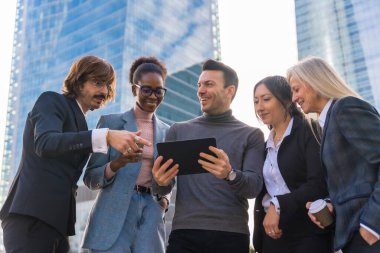 A group of multi ethnic business people in a business park smiling looking at a tablet