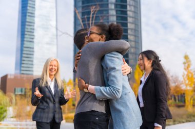 Middle-aged multi-ethnic businessmen and businesswomen giving each other a hug between colleagues
