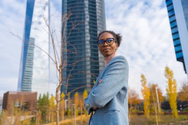 Portrait of black ethnic businesswoman or executive wearing glasses standing in business park, arms crossed