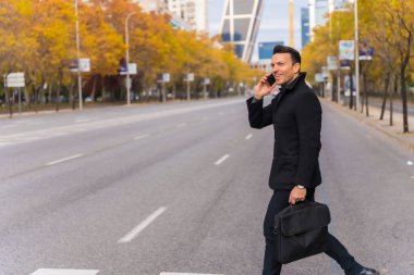 Middle-aged Caucasian businessman talking on the phone at a city zebra crossing