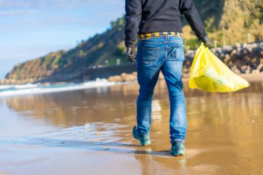 Sea pollution, unrecognizable person walking on the beach collecting plastics. ecology concept