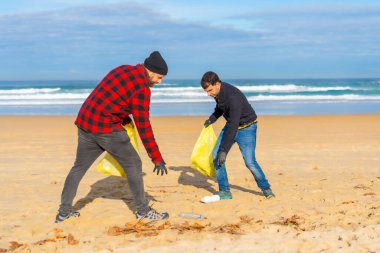 Two men collecting plastic on the beach. Ecology concept, sea pollution