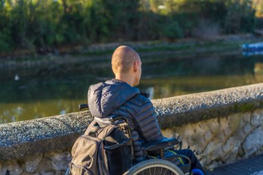 A disabled person in a wheelchair in a park at sunset next to a river