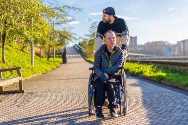 Smiling disabled person in a wheelchair walking with his brother in a park