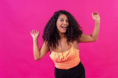 Curly-haired woman in summer clothes on a pink background dancing, studio shot