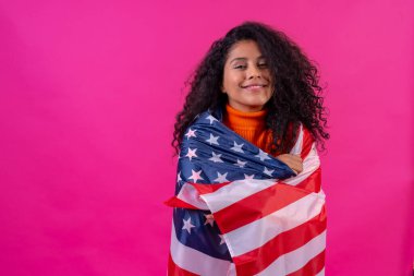 Portrait of a curly-haired woman smiling with the usa flag on a pink background, studio shot