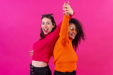 Female friends in sunglasses having fun and dancing on a pink background, studio shot, lifestyle