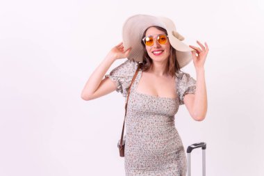 Vacation concept. Portrait of a smiling young tourist woman with suitcase and hat on a white background