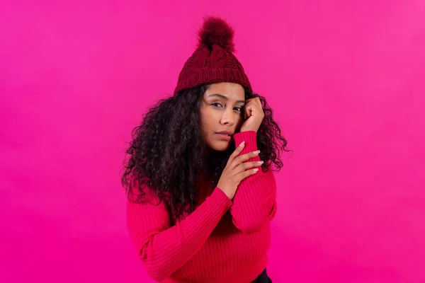 Curly-haired woman in a woolen cap on a pink background portrait with cold, studio shot