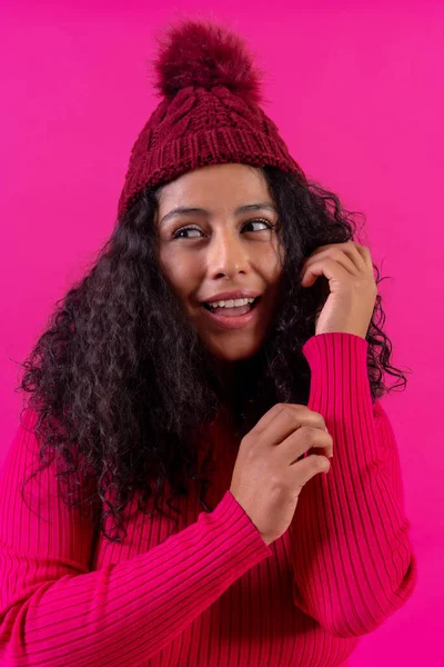 Curly-haired woman in a wool cap on a pink background portrait smiling, studio shot