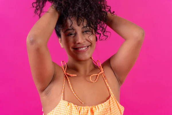 Portrait of a curly-haired woman in summer clothes on a pink background, studio shot