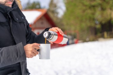 Man drinking coffee from a hot thermos in winter in the snow