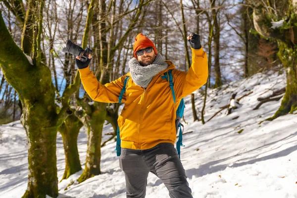 Portrait of a photographer trekking with a backpack taking photos in a beech forest with snow, fun and winter hobbies