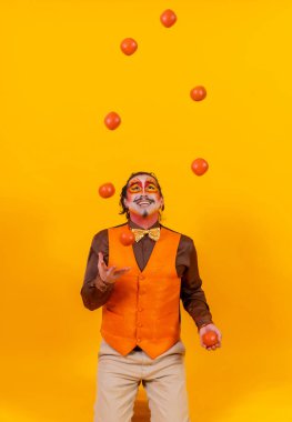 Portrait of a juggler in a vest with a painted face juggling balls on a yellow background