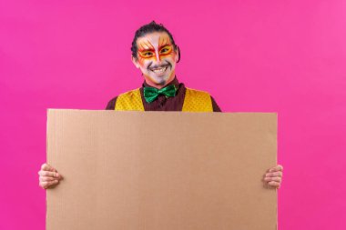 Clown with white facial makeup showing a sign on a pink background, announcing something