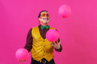 Clown with white facial makeup on a pink background, juggling balls