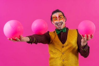 Clown with white facial makeup on a pink background, juggling balls