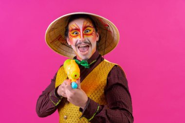 Clown with white facial makeup on a pink background, playing with toy guns