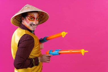 Clown with white facial makeup on a pink background, with toy guns