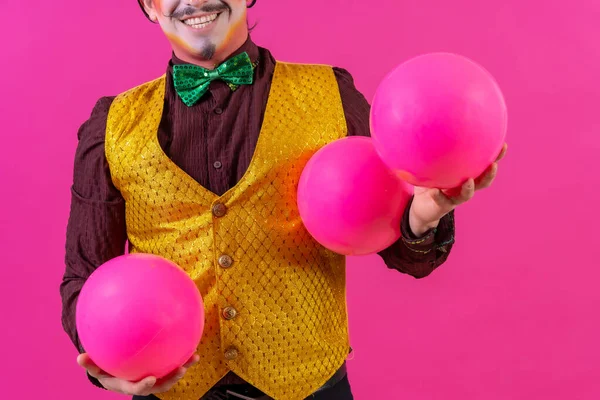Clown with white facial makeup on a pink background, juggling balls