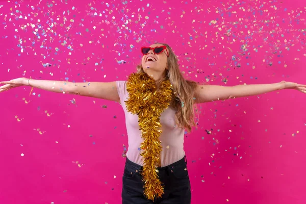 Young blonde caucasian woman partying, in the disco having fun throwing confetti, isolated on a pink background
