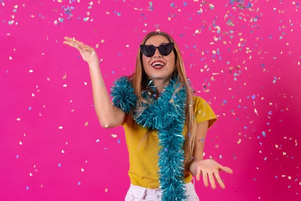 Young blonde caucasian woman partying, in the disco having fun throwing confetti, isolated on a pink background