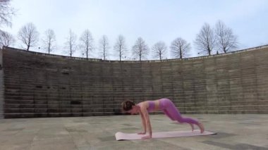 Burpees, caucasian young woman doing fitness in a city park, warming up pre exercise on the mat