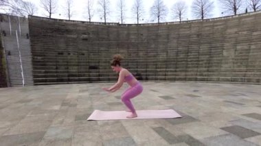 Burpees, caucasian young woman doing fitness in a city park, warming up pre exercise on the mat
