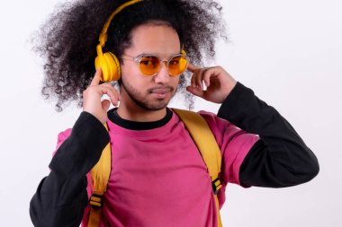 Portrait with pink t-shirt and backpack listening to music online. Young man with afro hair on white background