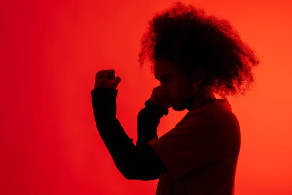 Silhouette with red light of boxer attacking. Young man with afro hair on white background