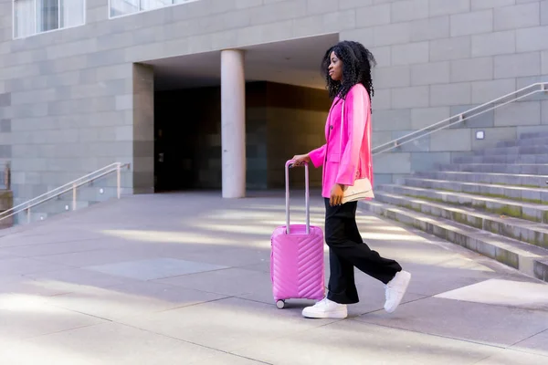 African american young woman in the city, portrait of a young woman in pink jacket walking with a suitcase