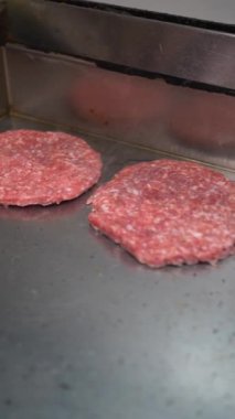 A cook frying the burgers on the griddle in the kitchen of the bar or restaurant