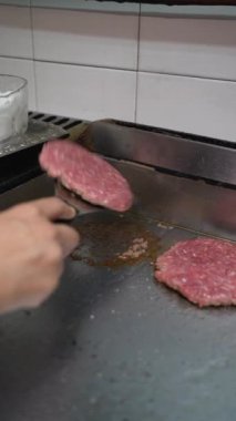 A cook frying the burgers on the griddle in the kitchen of the bar or restaurant