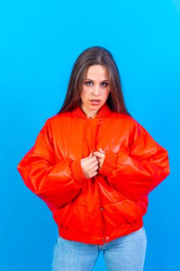 Close up portrait of young caucasian woman in red windbreaker isolated on blue studio background