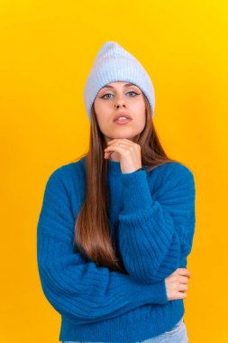 Close up portrait of young caucasian woman in blue wool sweater isolated on yellow background in studio