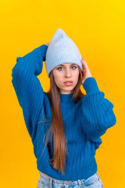 Close up portrait of young caucasian woman in blue wool sweater isolated on yellow background, wearing wool cap