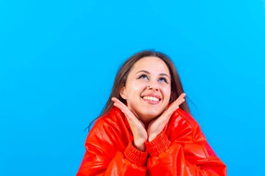 Close up portrait of a young woman, cheerful or laughing isolated on blue studio background in red windbreaker