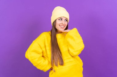 Close up portrait of a young, cheerful woman isolated on purple studio background in yellow woolen pullover