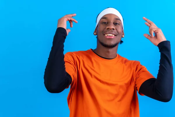 Black ethnic man in orange clothes on a blue background, having fun dancing