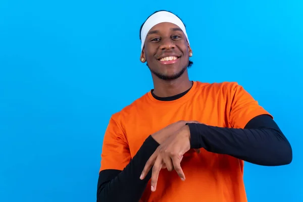 Black ethnic man in orange clothes on a blue background having fun smiling and dancing