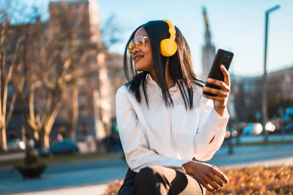 African american woman listening to music with headphones at sunset in the city, online music