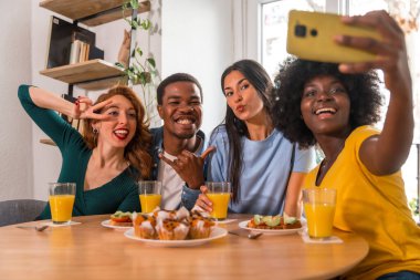 Kahvaltıda, evde portakal suyu ve kek yiyip selfie çeken çok ırklı arkadaşlar.