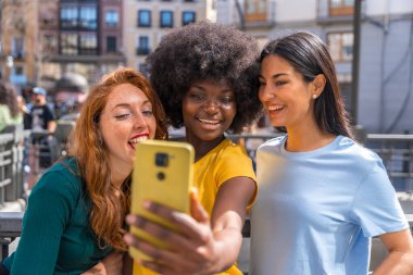 Şehirde selfie çeken üç çok ırklı genç kadın, arkadaşlık konsepti, feminizm.
