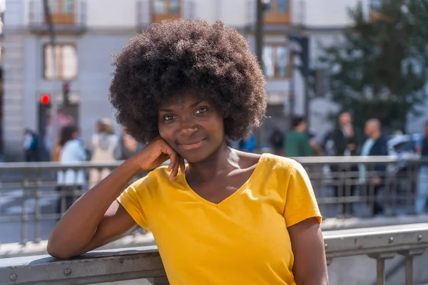 Black woman with afro hair in yellow t-shirt smiling in the city, lifestyle