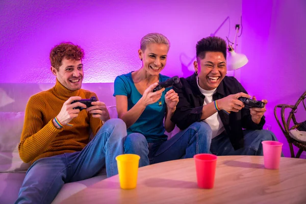 stock image Group of young friends play video games together on the sofa at home, purple led