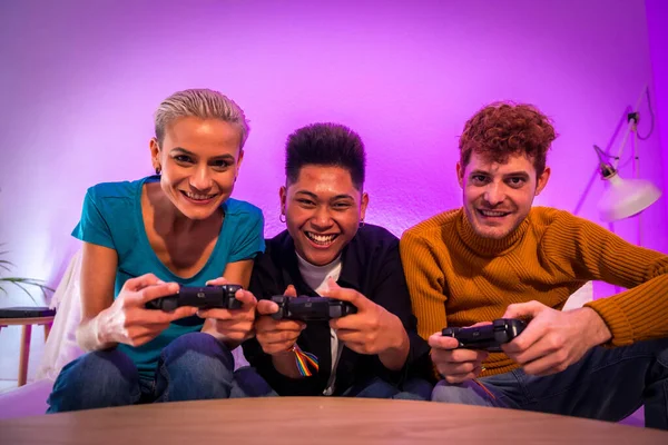 stock image Group of young friends playing video games together on the sofa at home, purple led, competing looking at camera