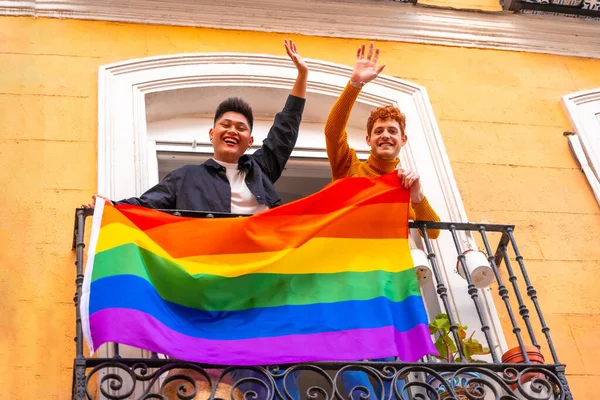 男同性恋情侣们在家里的阳台上挂着Lgbt国旗 微笑着 Lgbt骄傲 — 图库照片