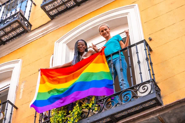 男女同性恋 双性恋和变性者自豪地微笑着在家中派对的阳台上挂着Lgbt国旗的女同性恋者 — 图库照片